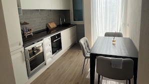 A modern kitchen with white cabinets, a built-in oven, and a dining area with a table and chairs.