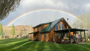A log cabin with a porch and outdoor seating area, surrounded by a grassy field and trees. - Modern Log Cabin on a historic cattle ranch in Northern Nevada.  (Winnemucca)