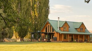A log cabin with a porch, large windows, and a green roof. - Modern Log Cabin on a historic cattle ranch in Northern Nevada.  (Winnemucca)