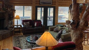 A cozy cabin interior with a stone fireplace, leather sofas, a coffee table, and a large tree trunk centerpiece. - Modern Log Cabin on a historic cattle ranch in Northern Nevada.  (Winnemucca)