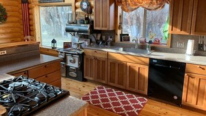 A cozy cabin-style kitchen with wooden cabinets, a stove, and a dishwasher. - Modern Log Cabin on a historic cattle ranch in Northern Nevada.  (Winnemucca)