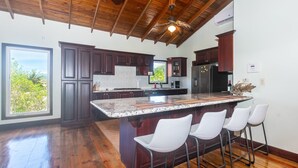 A spacious kitchen with dark wood cabinets, a large island with bar stools, and a view of greenery outside. - Shore Thing!  Unique and spacious 3-bedroom waterfront - Coco View (Roatan)