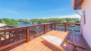 A wooden deck with a lounge chair and a view of a lake and trees. - Shore Thing!  Unique and spacious 3-bedroom waterfront - Coco View (Roatan)