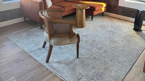 A cozy living room with a brick wall, a wooden ceiling, a large window, a sofa, a chair, a coffee table, and a floor lamp.
