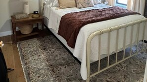 A bedroom with a bed, a nightstand, a lamp, a ceiling fan, and a window with curtains.