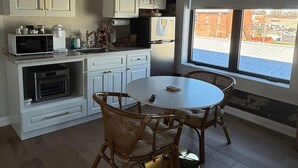 A kitchen with white cabinets, a dining table with wicker chairs, a microwave, a refrigerator, and a window with a view of a parking lot.