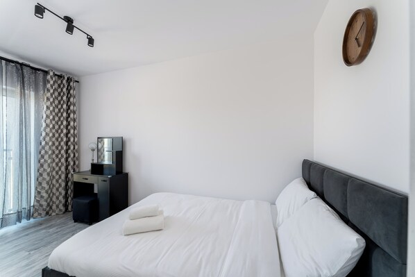 A hotel room with a bed, a desk, a TV, and a clock on the wall.