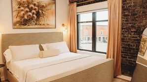 Een net opgemaakt bed met hoofdeinde, een groot raam met gordijnen en een bakstenen muur.