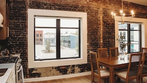 Een eetgedeelte met een bakstenen muur, een groot raam, een kroonluchter en een houten tafel met stoelen.