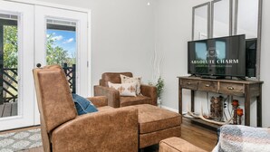 Una sala de estar con un sofá de cuero marrón, un televisor sobre un mueble de madera y un ventanal corredero que da a un área exterior.