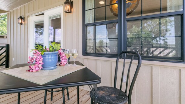 Un patio cubierto con una mesa, sillas, una planta en maceta y una ventana con detalles decorativos.