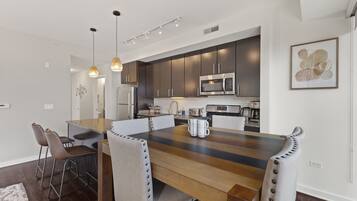 A modern kitchen with dark cabinets, stainless steel appliances, and a wooden dining table with chairs.