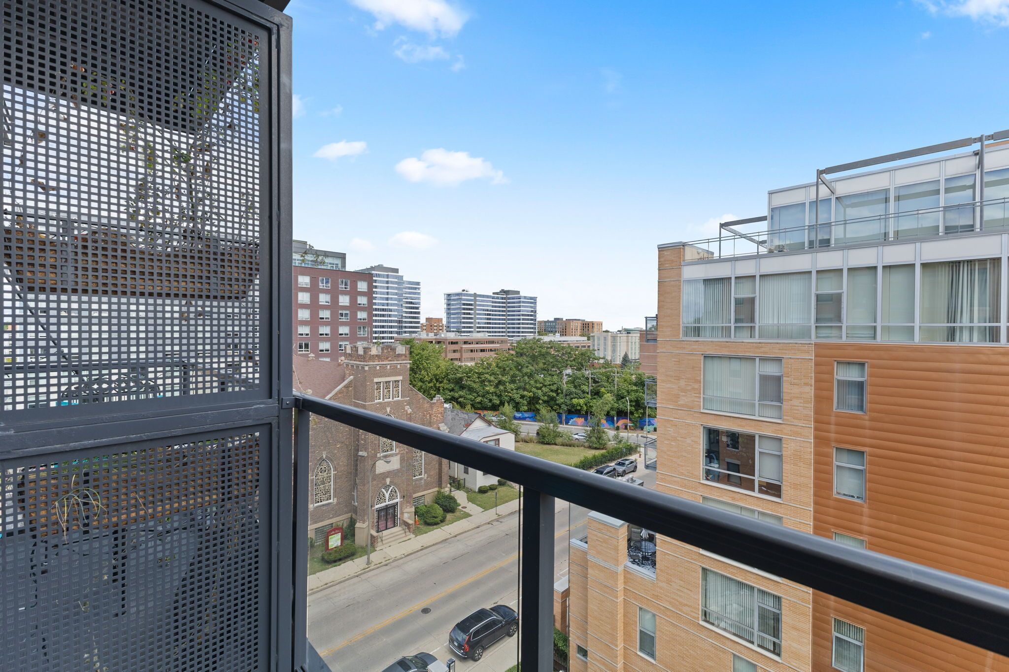 Un edificio de gran altura con varios pisos, ventanas amplias y vista a una calle con coches y árboles.
