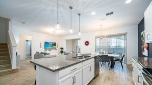 A modern kitchen with granite countertops, white cabinetry, and stainless steel appliances. There is a dining area with a table and chairs, and a large window providing natural light.