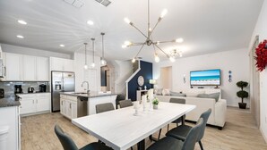 A modern kitchen with white cabinets, a central island, and a dining area with a white table and four chairs.