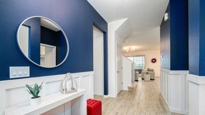 A hallway with a white console table, a red ottoman, a round mirror, and a blue wall.