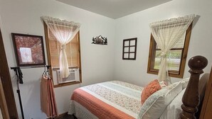 Un dormitorio con una cama, dos ventanas con cortinas, un cuadro en la pared y un adorno decorativo.
