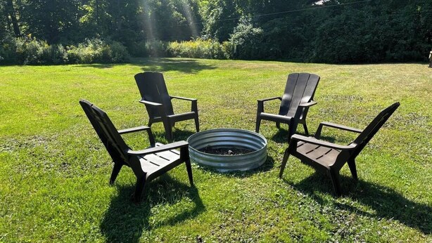 Un espacio al aire libre con césped y cuatro sillas Adirondack dispuestas en círculo alrededor de un brasero de metal.