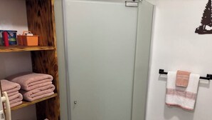Un baño con mampara de vidrio, un estante de madera con toallas dobladas y un perchero con una toalla a rayas.