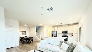 A modern living room with a white sofa, a coffee table, and a dining area with a table and chairs. There is a kitchen with white cabinets and appliances. - Luxurious Summerlin Townhome,BEDROOM downstairs/Loft UP with STRIP&CITY VIEWS!!! (Las Vegas)