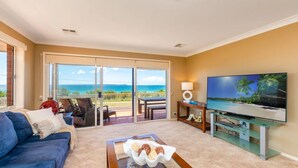 A living room with a sofa, a coffee table with snacks, a TV, and a balcony with a view of the ocean. - Palms on Collingwood by Experience Jervis Bay (Vincentia)