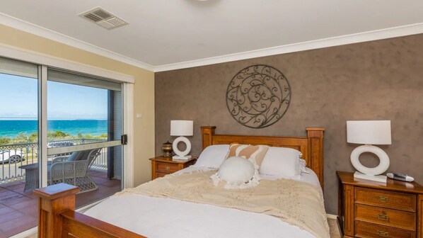 Un dormitorio con una cama grande, dos mesitas de noche con lámparas, un adorno en la pared y un balcón con vista al océano.