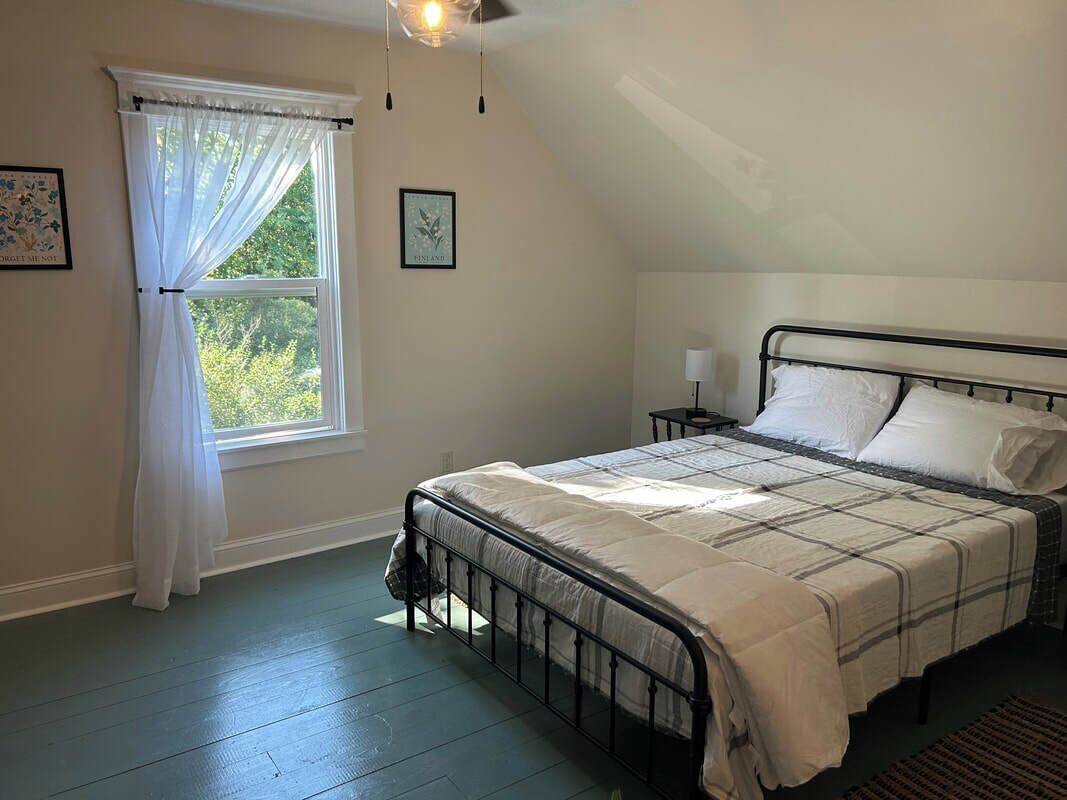 A bedroom with a bed, a window with curtains, a nightstand, and a ceiling fan.