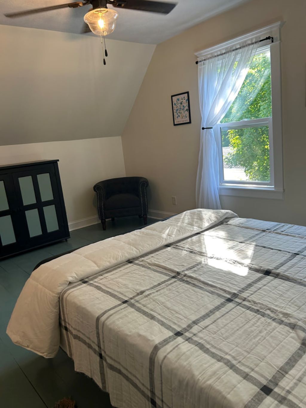 A bedroom with a bed, a ceiling fan, a window with curtains, and a chair.