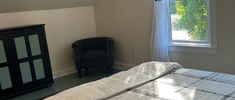 A bedroom with a bed, a ceiling fan, a window with curtains, and a chair.