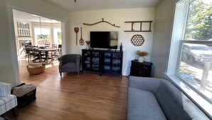 Una sala de estar con un sofá, un televisor, una zona de comedor con sillas y suelo de madera.