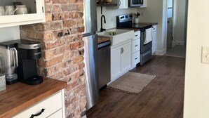 Una cocina con armarios blancos, pared de ladrillo, microondas, cafetera y lavavajillas.