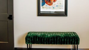 A room with a framed artwork of a guitar player, a green velvet bench, and a wooden floor. - The Aaron is a charming 2-bedroom/ 2 bathroom apartment.  (Leitchfield)