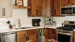 A kitchen with wooden cabinets, a stainless steel dishwasher, a microwave, a stove, and a round wooden table with stools. - The Aaron is a charming 2-bedroom/ 2 bathroom apartment.  (Leitchfield)