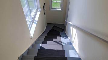 Uma escadaria com corrimão, uma pequena janela no topo e uma porta na base.