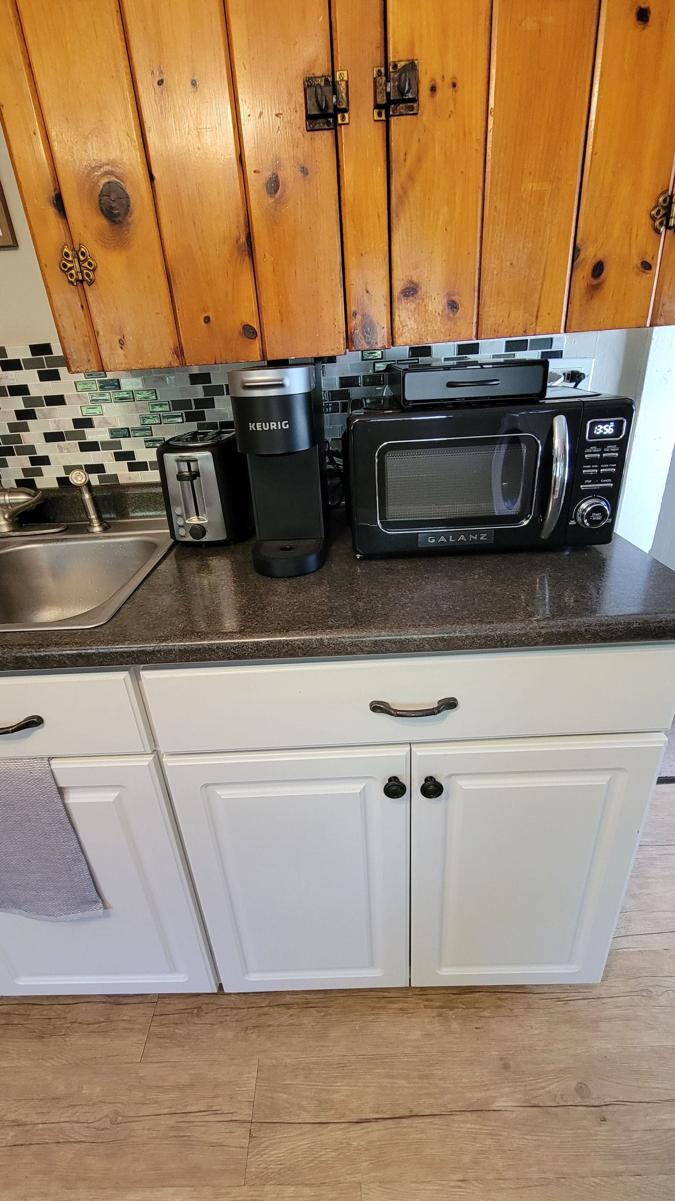 Una cocina con armarios blancos, microondas negro, tostadora y cafetera sobre la encimera.