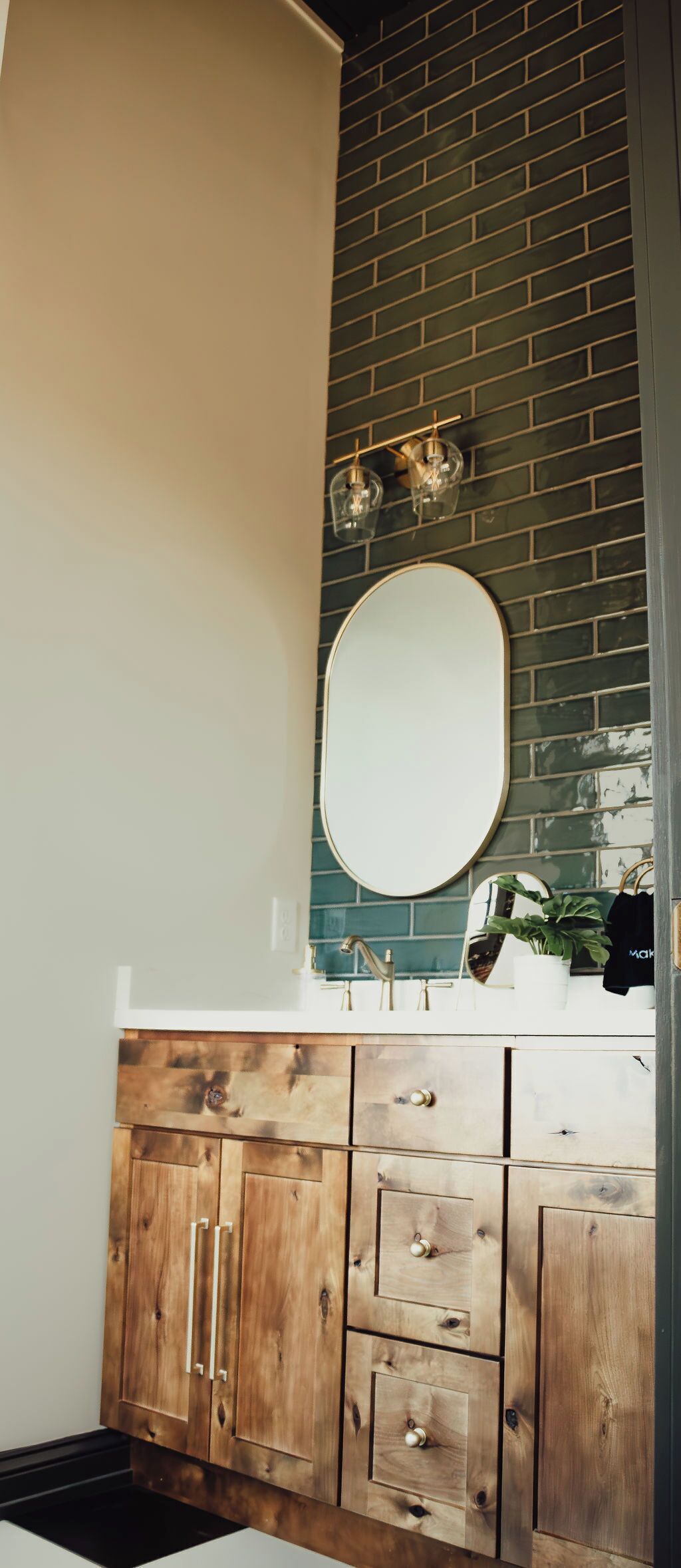 Un baño con tocador de madera, un espejo redondo y pared con azulejos verdes.
