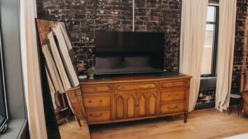 Une pièce avec un mur en briques, une commode en bois dotée de tiroirs, un téléviseur à écran plat posé sur le dessus, et une fenêtre avec des rideaux.