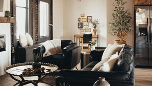 A modern living room with a black leather sofa, a wooden coffee table, and a dining area with a wooden table and chairs.