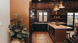 A modern kitchen with dark cabinetry, a central island, and a brick wall.