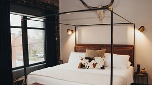A four-poster bed with a cowhide pillow, a wooden bench, and a cow skull on the wall.