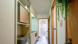 A narrow hallway with a metal trash bin, a wooden door with a green hanging plant, and a view into another room through a frosted glass door. - Fukuoka Loft 203  (Fukuoka)