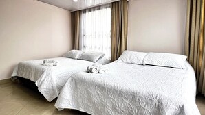 A hotel room with two single beds, a large window with curtains, and a tiled floor.