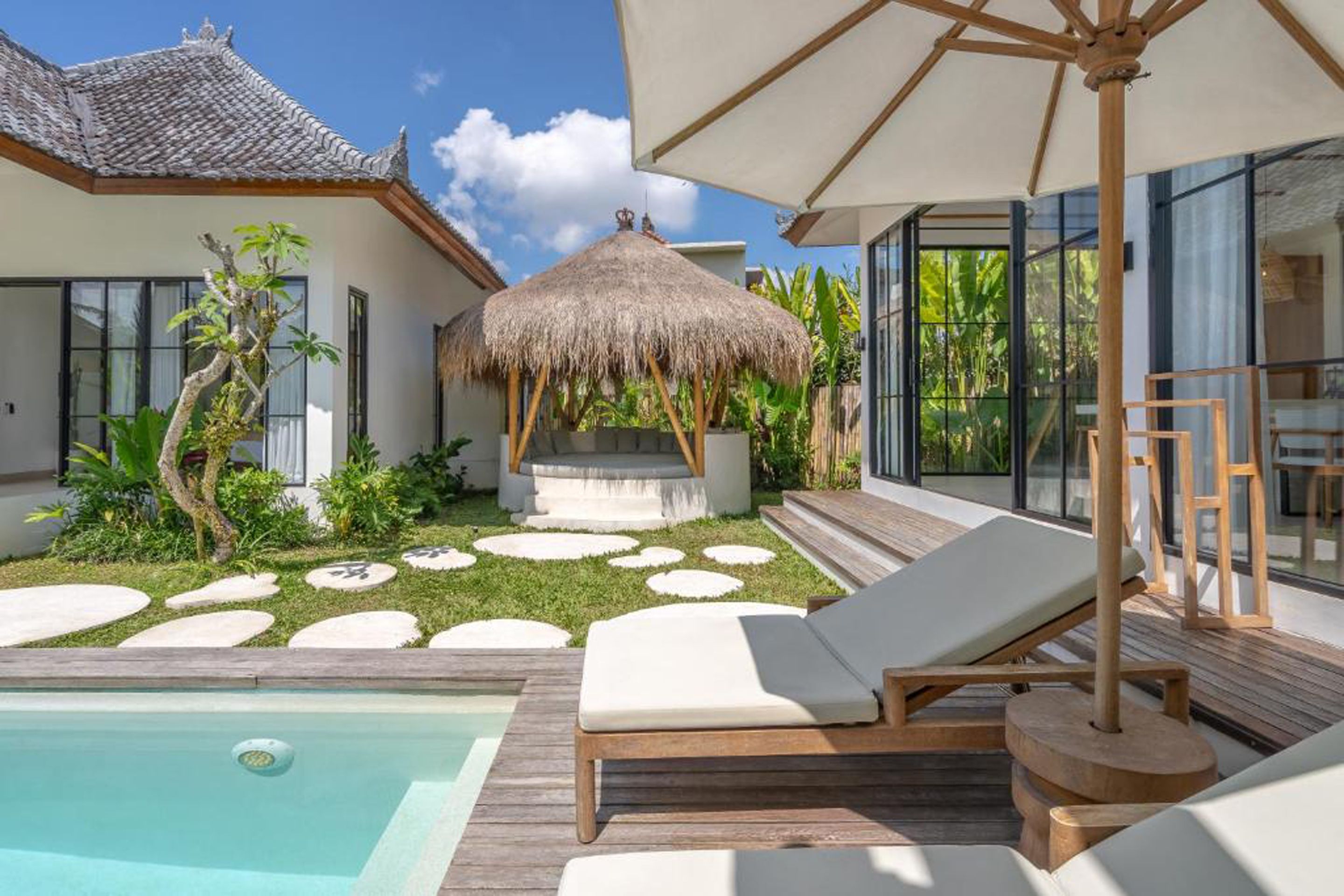 Ein Poolbereich mit Liegestühlen, einer Strohdachkonstruktion und einem Garten mit trittfesten Steinen.