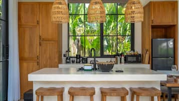Una cocina moderna con una isla grande, taburetes de bar de madera y vistas a exuberante vegetación a través de la ventana.