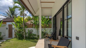 A covered outdoor seating area with two chairs, a concrete pathway, and lush greenery including banana plants. - Beta Villa by Betterplace (Ubud)