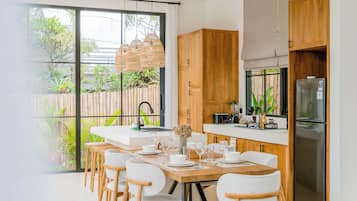 Eine moderne Küche mit Holzschränken, einem Edelstahlkühlschrank und einem Essbereich mit weißen Stühlen und einem Holztisch.