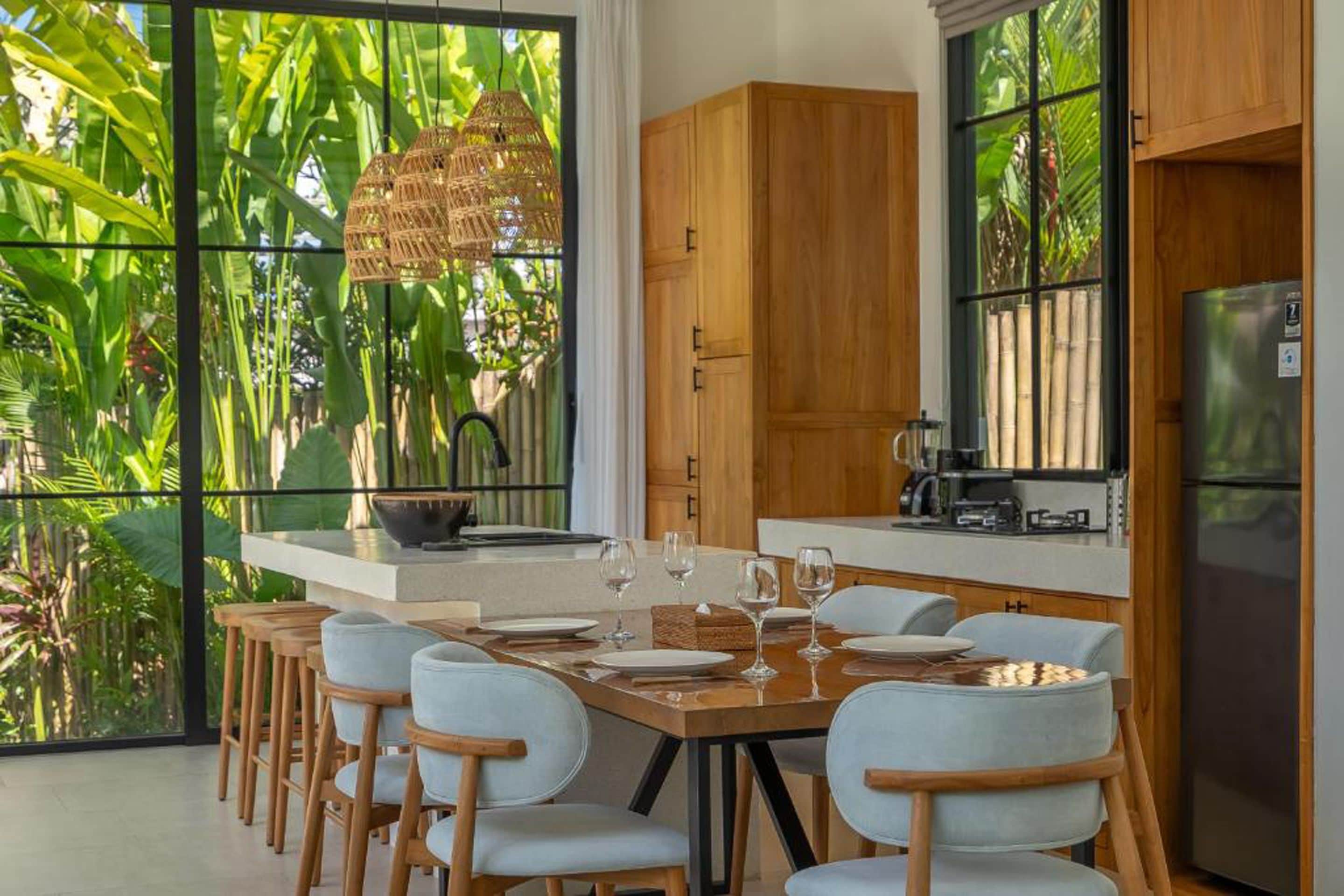 Cocina moderna con comedor, ventanas amplias y vista a plantas tropicales.