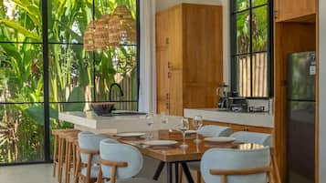 Cocina moderna con comedor, ventanas amplias y vista a plantas tropicales.