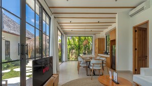 A modern living room with a large TV, dining area, and a view of a tropical garden. - Beta Villa by Betterplace (Ubud)