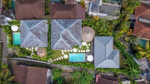 An aerial view of a residential area with multiple houses, a swimming pool, and a garden with a circular stone pattern.